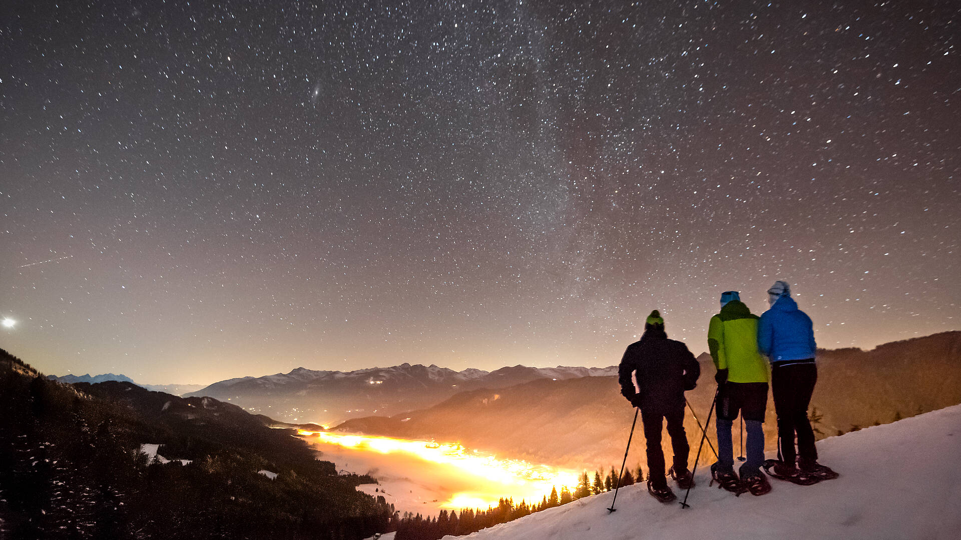 Winterwanderer genießen den Sternenhimmel über dem Weissensee in verschneiter Wintelandschaft.